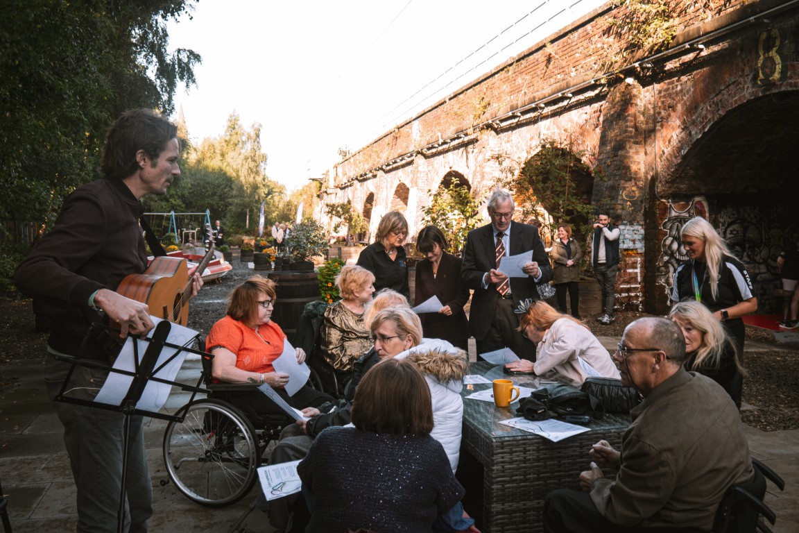 A musician plays for a group seated in the garden
